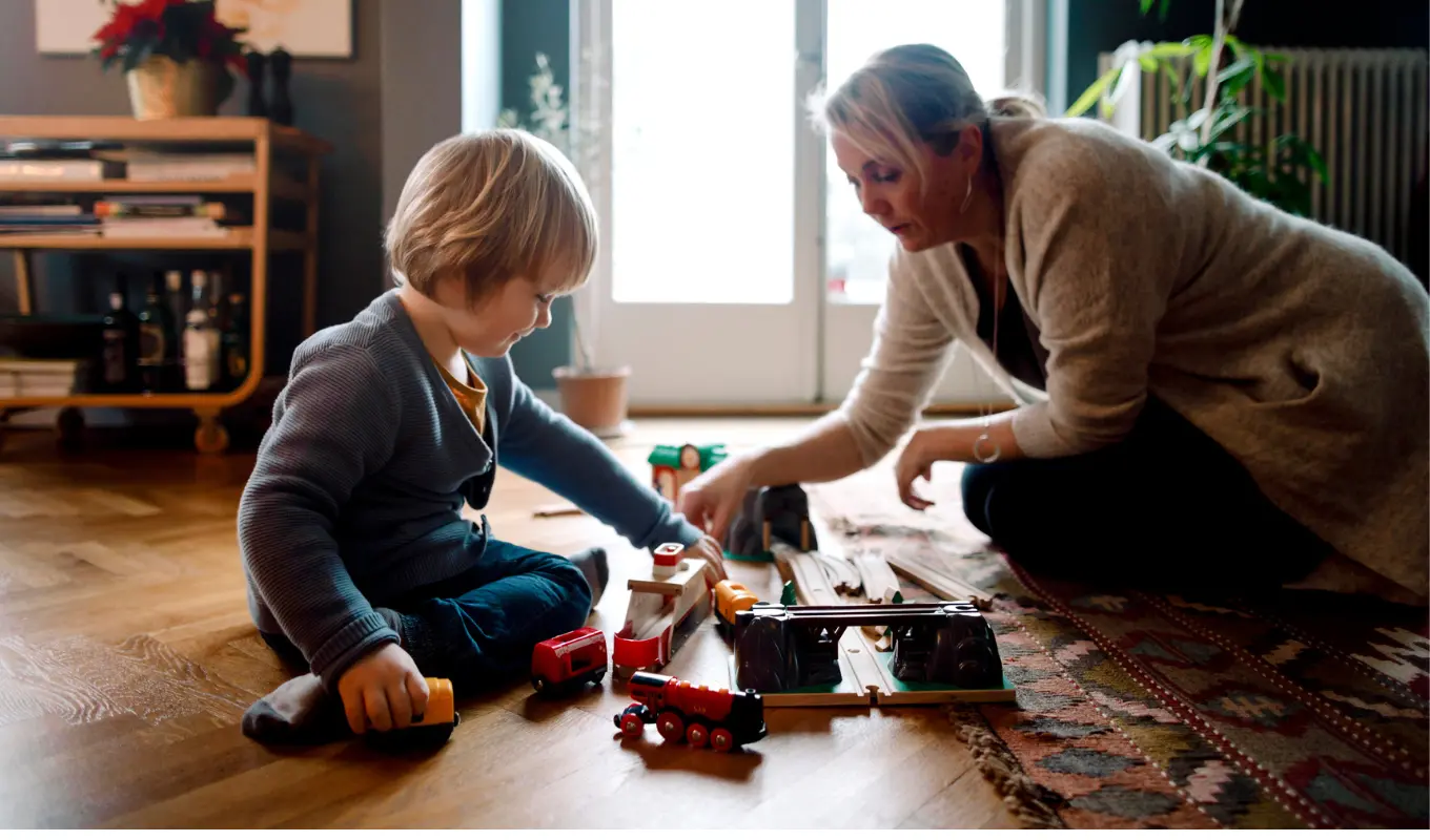 Mor och barn leker med leksakståg när de sitter på trägolv i vardagsrummet
