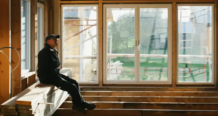 Äldre man sitter på golvbjälkar i ett nybyggt hus 