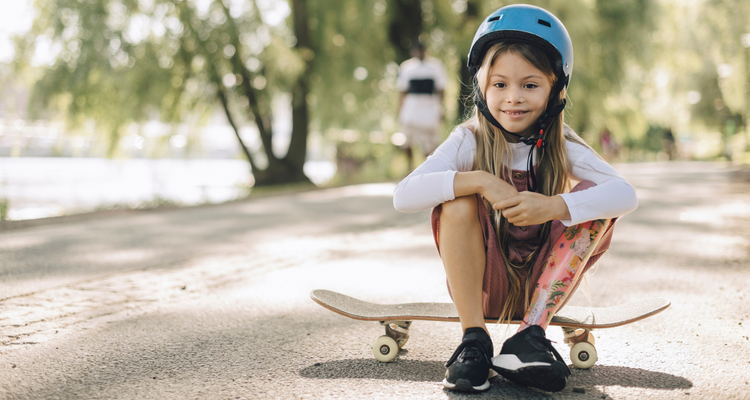 Flicka med benprotes sitter på en skateboard i parken och tittar in i kameran